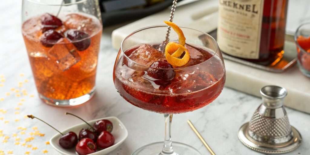 A stylish cocktail glass with a cherry bounce-based drink, garnished with fresh cherries and set against an elegant background.