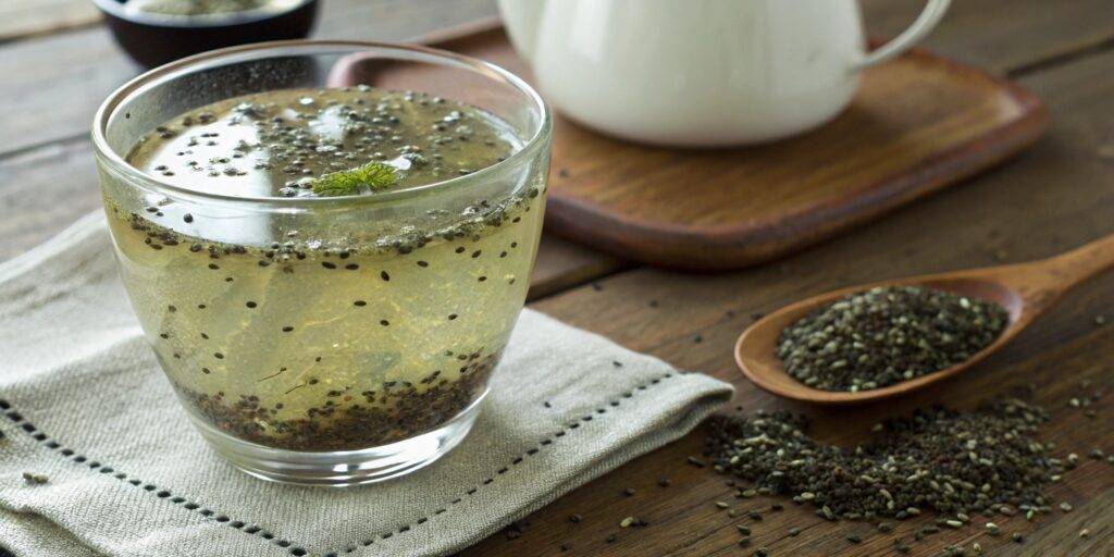 A glass of chia-infused herbal tea with chia seeds floating inside, garnished with a sprig of mint and a lemon slice.